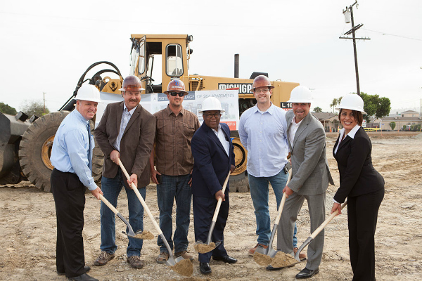 A team of 7 standing in front of a tractor and holding shovels ready to break ground on Avaire South Bay development site.