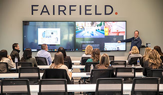 A diverse group of Fairfield associates watch a presentation on to large televisions about the importance of the company's culture and values.