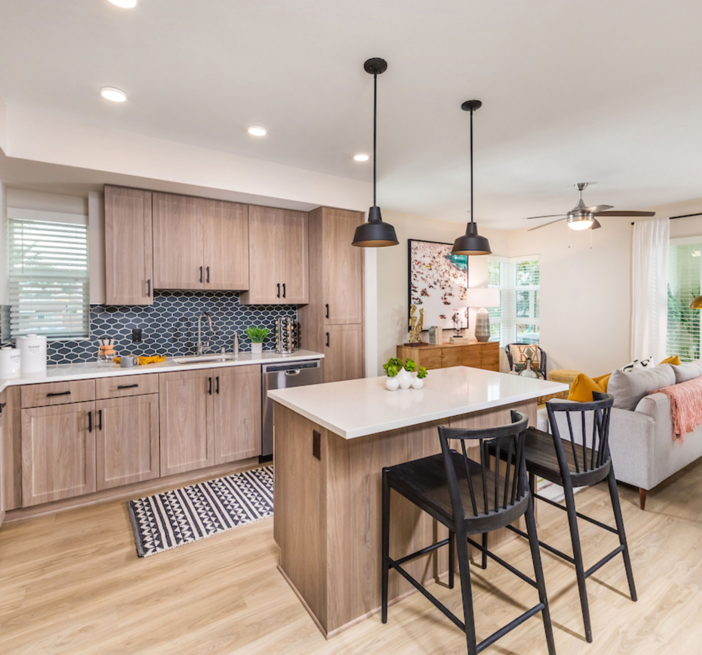 A bright kitchen with a kitchen island, stools, and wooden cabinets leads into the living room.