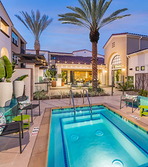 A hot tub with poolside seating and patio lighting at dusk looking towards two palm trees in one of Fairfield's apartment communities.