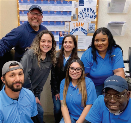 7 diverse associates wearing blue Fairfield polos smiling in their breakroom.